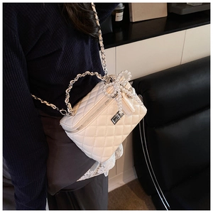 Detail showing white quilted leather texture with pearl bow charm and silver chain strap