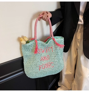 Detail view of woven straw bag with pink Swim and Tonic embroidery and tassel accents