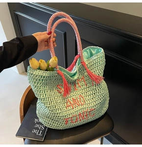 Close-up of mint green straw tote bag with pink tassel and Swim and Tonic embroidery