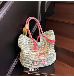 Detailed view of hand-woven mint green straw bag with pink embroidered text and tassel handles