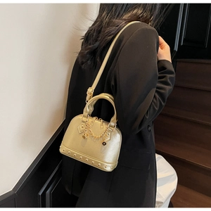 Dettaglio della borsa a conchiglia dorata con borchie metalliche e catena decorativa