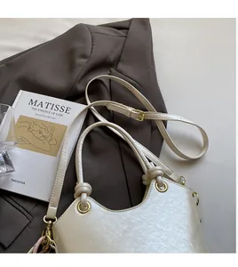 Détail d'un sac seau crème avec texture grainée, ferrures dorées et longue bandoulière