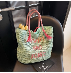 Detail of mint green straw bag featuring pink embroidery and striped woven handle with tassel