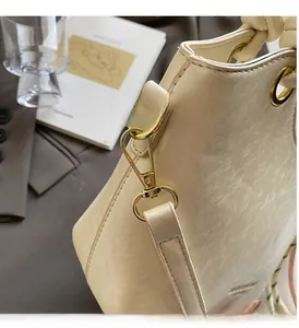 Détail du sac seau blanc cassé avec texture brillante et garnitures en métal doré