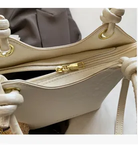 Détail de la fermeture éclair dorée lisse et de l'anse nouée du sac seau crème