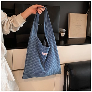 Detail of blue ribbed knit tote bag with pink patch tag shown in modern lifestyle setting