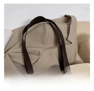 Close-up of woven straw tote bag featuring brown leather straps and golden stitching