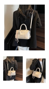 Detail view of cream Boston bag with embossed lettering and stylish woven tassel charm