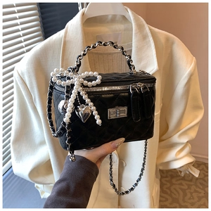 Detail of black quilted box bag with pearl bow charm and chain strap held by a model