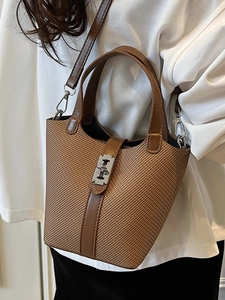 Brown woven bucket bag with leather handles and metallic buckle shown as crossbody style