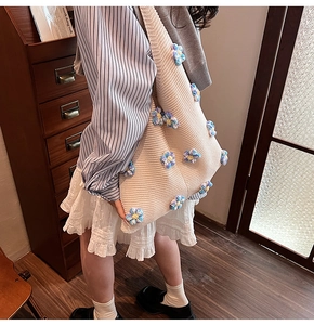Détail d'un sac cabas en tricot beige avec des fleurs au crochet bleues et jaunes en 3D