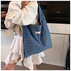 Blue striped canvas tote bag worn by a model in a casual lifestyle indoor setting