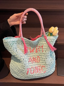 Mint green straw beach tote with pink embroidery and tassel on a wooden background