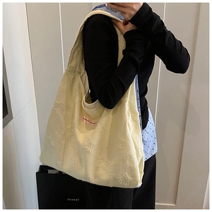 Detail of cream canvas tote bag featuring star jacquard texture and pink ribbon charm