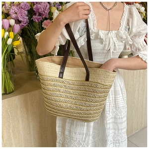 Detail view of woven straw tote bag with brown leather straps among fresh flowers