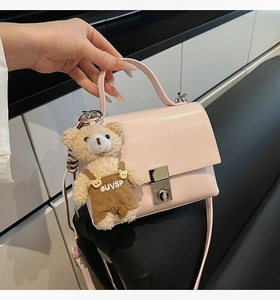 Detail of light pink crossbody bag with silver buckle and plush bear pendant accessory