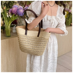 Detail view of large straw tote bag with brown leather straps and hollow stripe patterns
