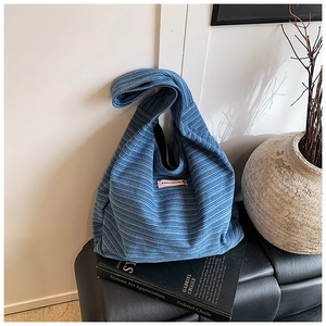 Detail view of blue striped corduroy tote bag with pink woven label on a black leather bench