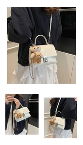Detail showing white glossy handbag with silver twist lock and cute teddy bear charm