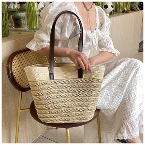 Detail of a large woven straw tote bag with brown leather handles on a vintage chair