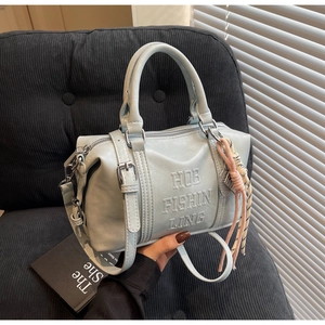 Detail of light blue faux leather bowling bag featuring embossed letters and woven charm