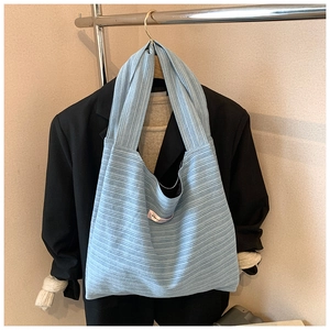 Macro shot of light blue striped tote bag with pink label paired with a black blazer