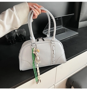 Détail d'un sac bowling en cuir gris avec texture tressée et charm d'ours décoratif