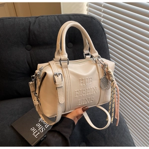 Creamy leather bowling bag with embossed lettering and tennis racket charm on sofa