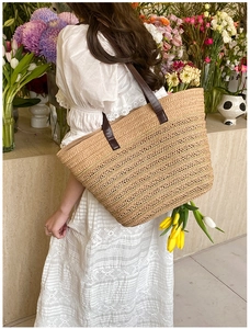 Detail of a large straw tote bag with brown leather handles and striped woven texture