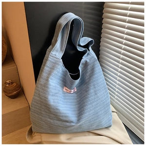 Detail of light blue knit tote bag with striped texture and pink woven label accent