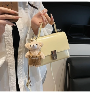 Detail of a creamy yellow square handbag featuring a silver lock and cute bear charm