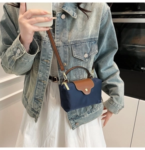 Detail of dark blue nylon mini bag with brown leather flap and golden metal clasp handle