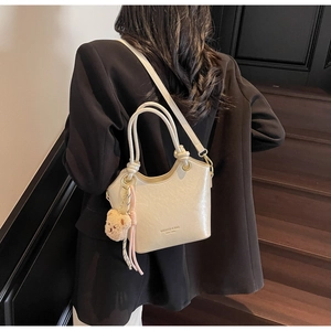 Détail du sac seau en similicuir crème avec poignée tressée et breloque ours en peluche