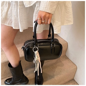 Vue détaillée du sac Boston en cuir noir avec pendentif à pompon et fermeture éclair