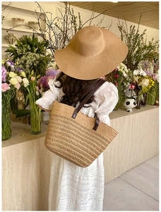 Detail of a woven straw tote bag with brown leather straps and matching wide-brim sun hat