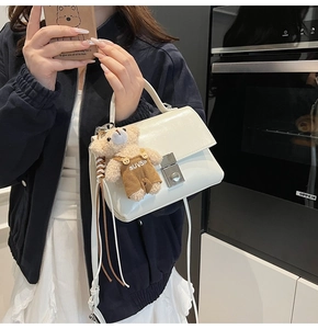 White flap handbag featuring a matte leather finish and a cute plush bear charm accessory