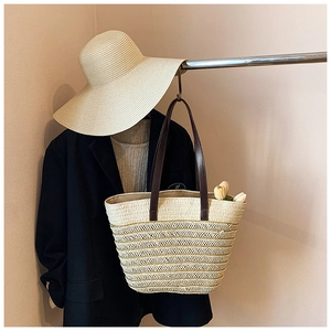 Detailed close-up of straw woven tote bag featuring dark brown leather straps and floral accents