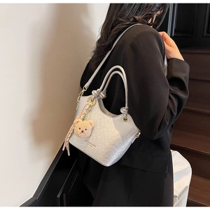 Détail d'un sac seau plissé argenté avec un pendentif ours en peluche sur le mannequin