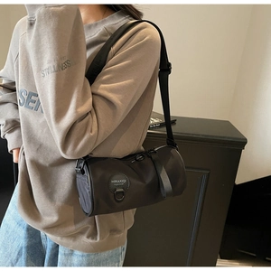 Detail view of the black cylindrical crossbody bag with circular brand logo on nylon fabric