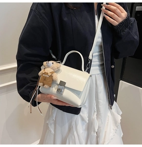 Close-up of white glossy crossbody bag with silver lock and a cute plush bear pendant