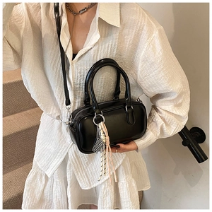 Sac bowling noir brillant porté par un modèle avec double anse et breloque tissée
