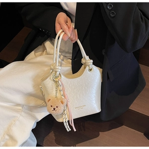 Détail du sac seau en similicuir beige avec poignée nouée et breloque ours en peluche