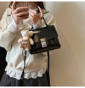 Detail of black glossy square handbag with silver twist lock and cute bear charm