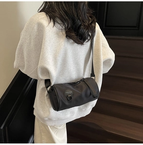 Close-up of a black cylindrical crossbody bag featuring a round logo patch on nylon material