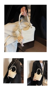 Close-up of white wavy pleated faux leather bucket bag with cute brown bear keychain charm
