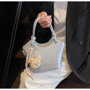 Détail du sac seau en PU argenté métallisé avec bord ondulé et pendentif ours en peluche