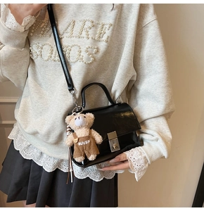 Close-up of black patent leather crossbody bag with silver buckle and plush bear charm