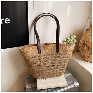 Detail showing handwoven natural straw tote with brown faux leather straps for summer beach use
