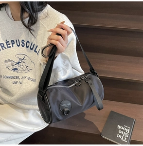 Close-up of black cylinder oxford cloth crossbody bag with silver zipper and logo detail