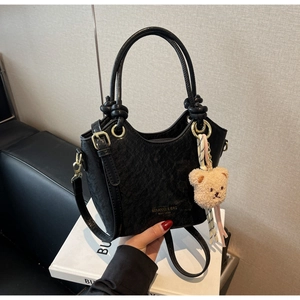 Détail du sac seau noir en PU texturé avec boucles dorées et breloque d'ours en peluche